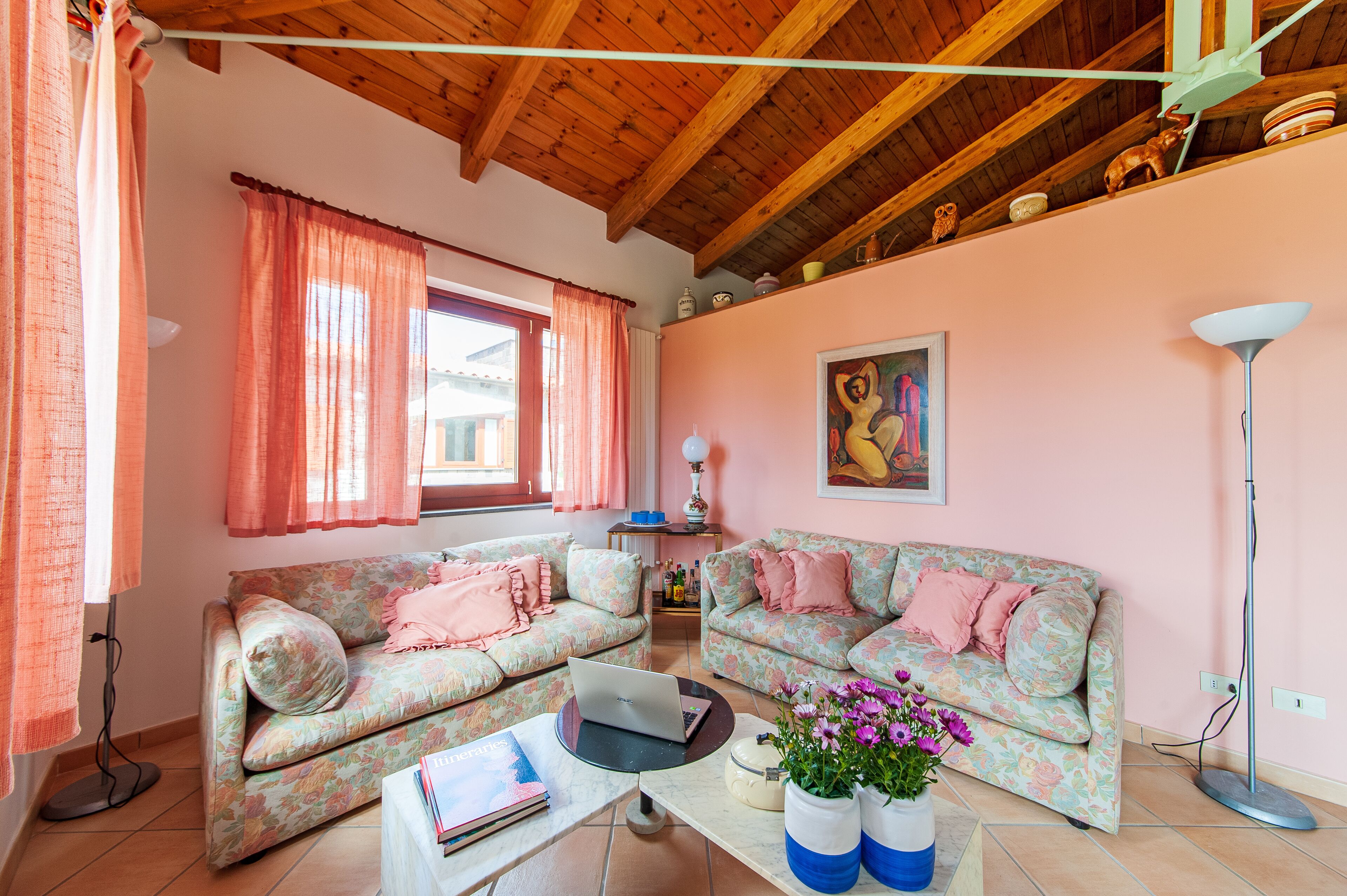 A living room with floral-patterned sofas, a coffee table with a laptop, and a vase with flowers.