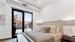 A modern bedroom with a large bed, a bench, a nightstand, and a view of the outside.