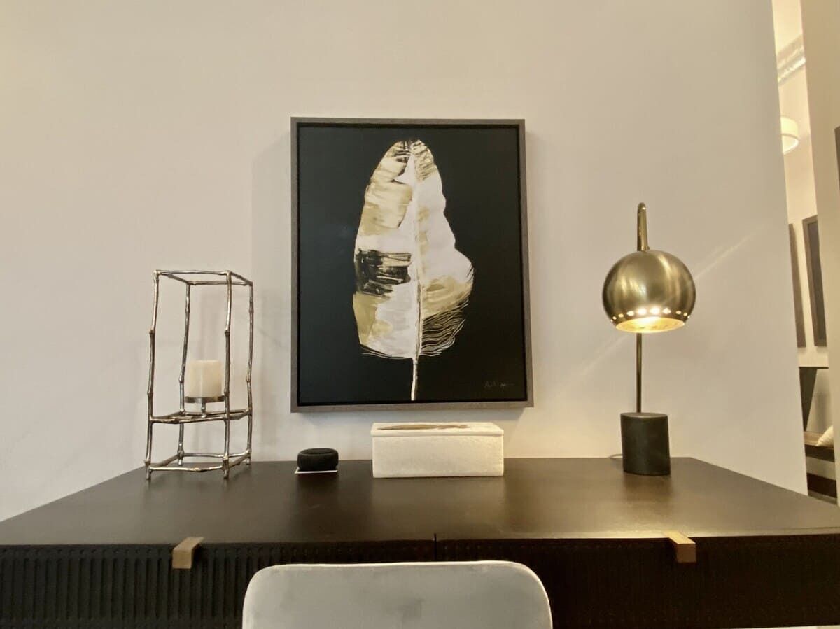 A desk with a framed artwork, a metal candle holder, a small box, and a floor lamp.