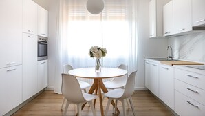 Une cuisine moderne avec des meubles blancs, une table de salle à manger ronde entourée de chaises, un vase de fleurs et un luminaire suspendu.