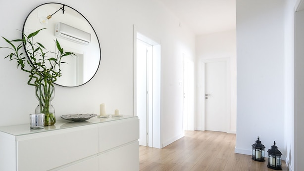 Une salle de bain moderne avec un meuble-lavabo blanc, un miroir rond, une plante en bambou et deux bougies.