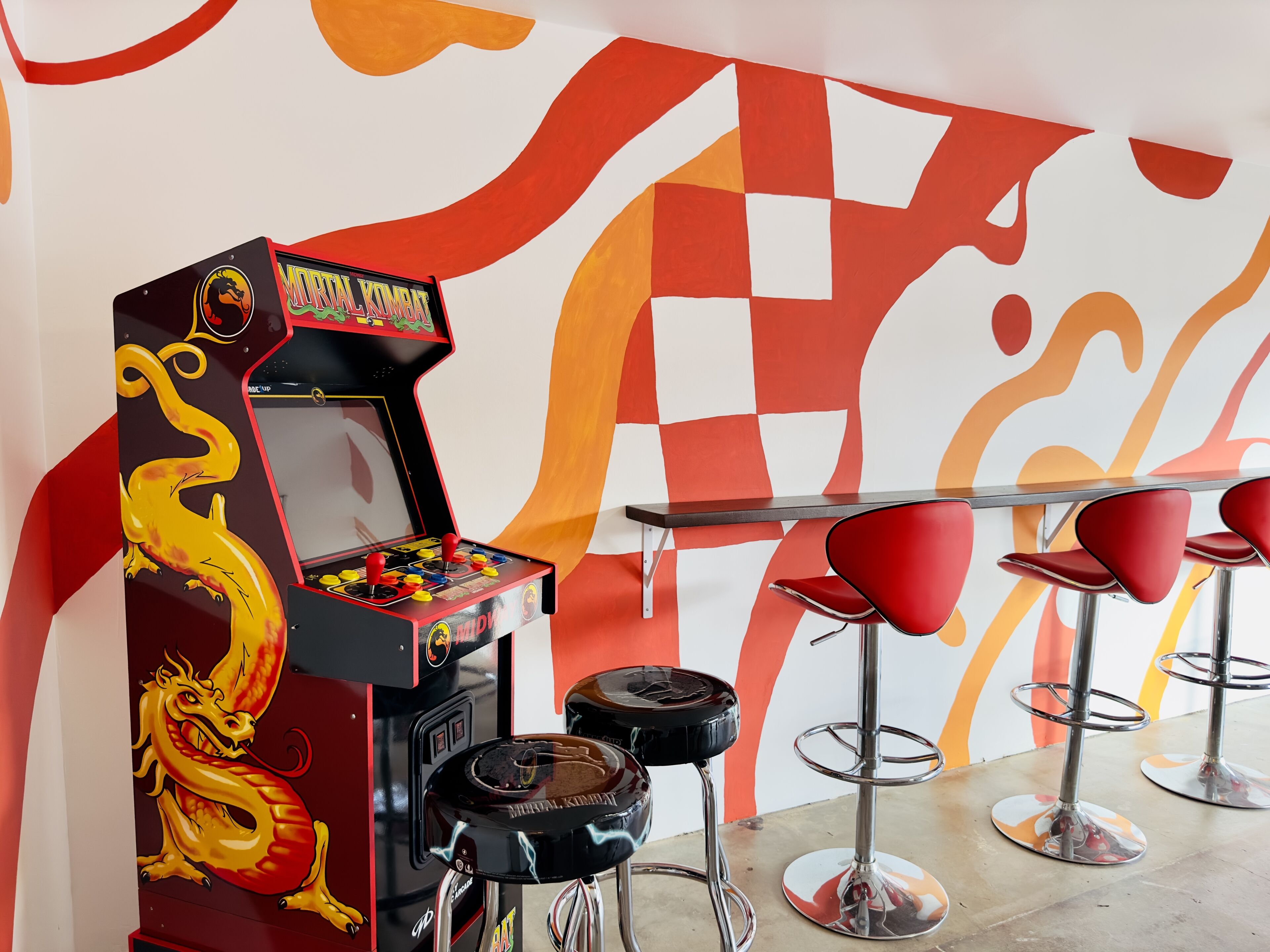 Een retro speelautomaat met een draakontwerp, een tafel en rode barstoelen.