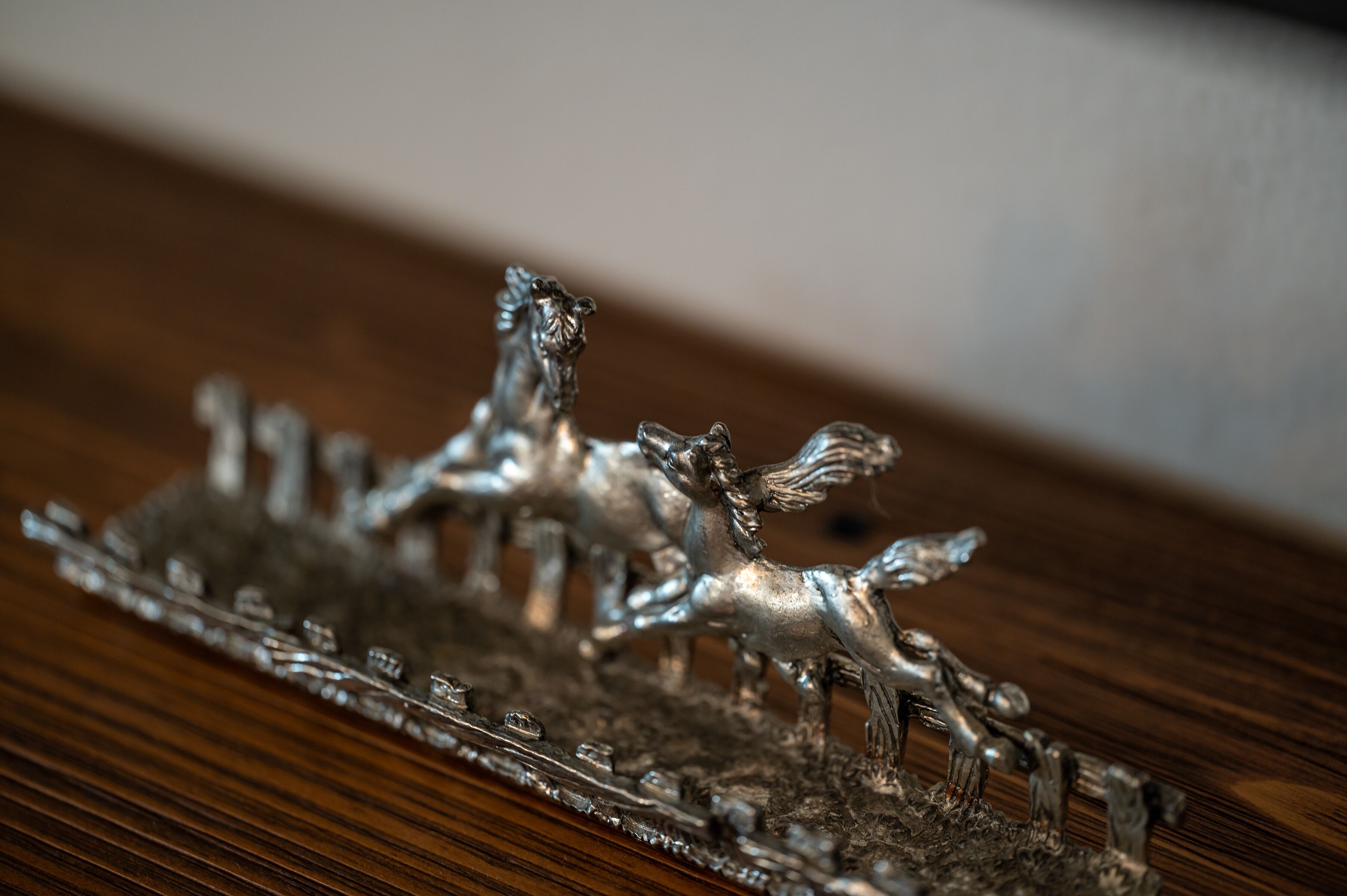 A close-up of a silver horse figurine on a wooden surface.