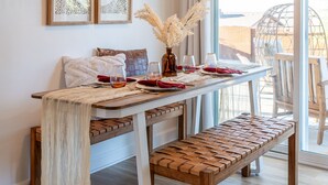 A dining area with a wooden table, bench, and hanging light fixture. - ★Hot tub under the stars★ 3 King Beds, Cowboy Pool, Desert Views, Fire Pit, EV (Twentynine Palms)