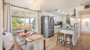 A modern kitchen with a large island, stainless steel appliances, and a dining area with a bench and table set for two. - ★Hot tub under the stars★ 3 King Beds, Cowboy Pool, Desert Views, Fire Pit, EV (Twentynine Palms)