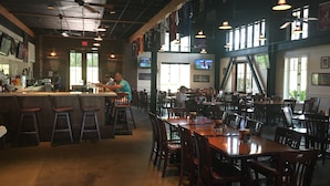 A spacious restaurant with high ceilings, exposed beams, and a mix of bar seating and tables. - Beach Club Resort. Book Your Summer Vacation Now! My Rates are Hard to Beat! (Gulf Shores)