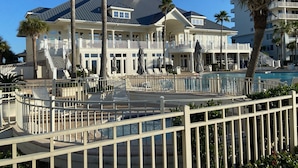 A large resort with multiple balconies, a swimming pool, and palm trees. - Beach Club Resort. Book Your Summer Vacation Now! My Rates are Hard to Beat! (Gulf Shores)