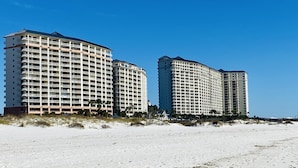 A beachfront hotel with multiple high-rise buildings, featuring balconies and a sandy beach in the foreground. - Beach Club Resort. Book Your Summer Vacation Now! My Rates are Hard to Beat! (Gulf Shores)