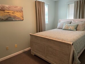Une chambre à coucher avec un lit, un tableau accroché au mur et une fenêtre avec des rideaux.