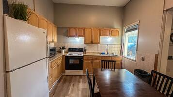 A kitchen with wooden cabinets, a stove, a refrigerator, and a dining table with chairs.