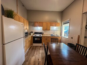 Une cuisine avec des meubles de rangement en bois, une cuisinière, un réfrigérateur et une table à manger avec des chaises.