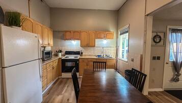 A kitchen with wooden cabinets, a refrigerator, stove, and a dining table with chairs.