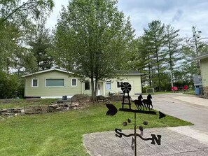 A green mobile home with a garage, a windmill, and a compass sign in the yard.