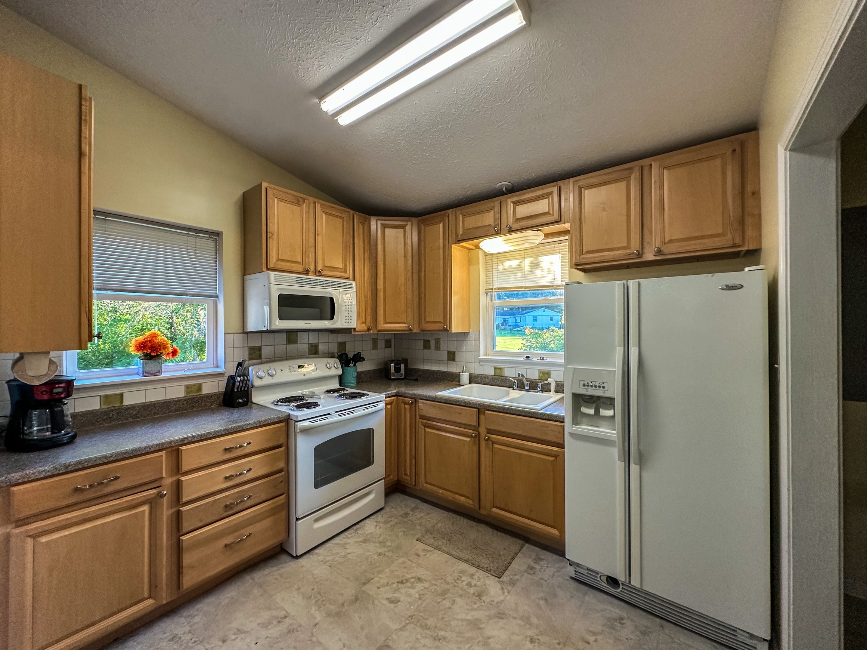 A kitchen with wooden cabinets, a white stove, a microwave, and a refrigerator.