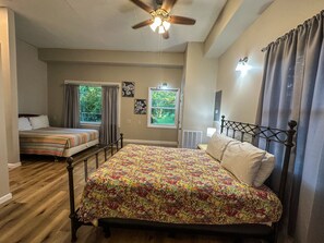 Une chambre avec un grand lit, un lit plus petit, un ventilateur de plafond et une fenêtre avec des rideaux.