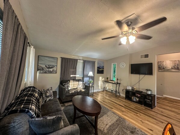 A living room with a sofa, a coffee table, a ceiling fan, a TV, and a fireplace.