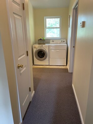 Une buanderie équipée d’un lave-linge et d’un sèche-linge, avec une fenêtre et un sol recouvert de moquette.