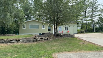 A single-story mobile home with a front porch, a small yard, and a paved driveway.
