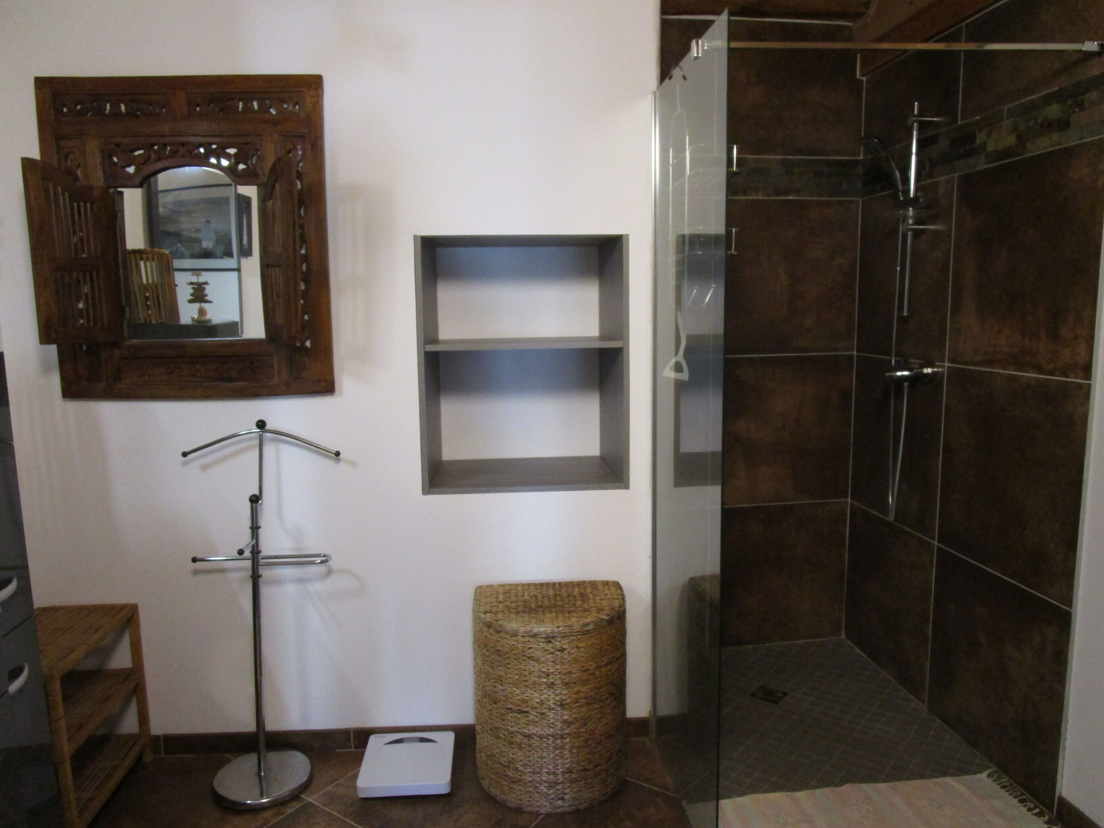 Une salle de bain avec un miroir à cadre en bois, une balance, un panier et une cabine de douche en verre.