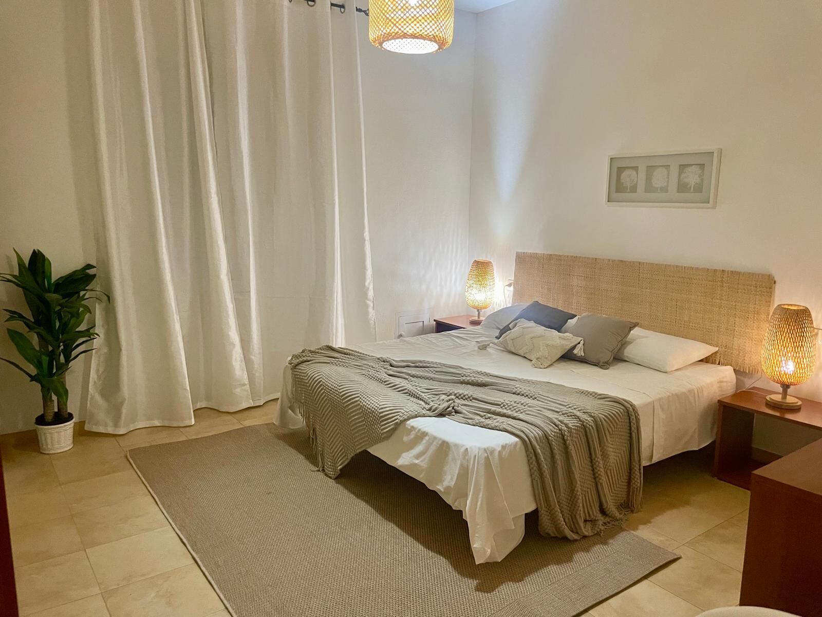 Ein Schlafzimmer mit einem Bett, zwei Nachttischlampen, einem Blumentopf, einem Teppich und einem Wandbild.