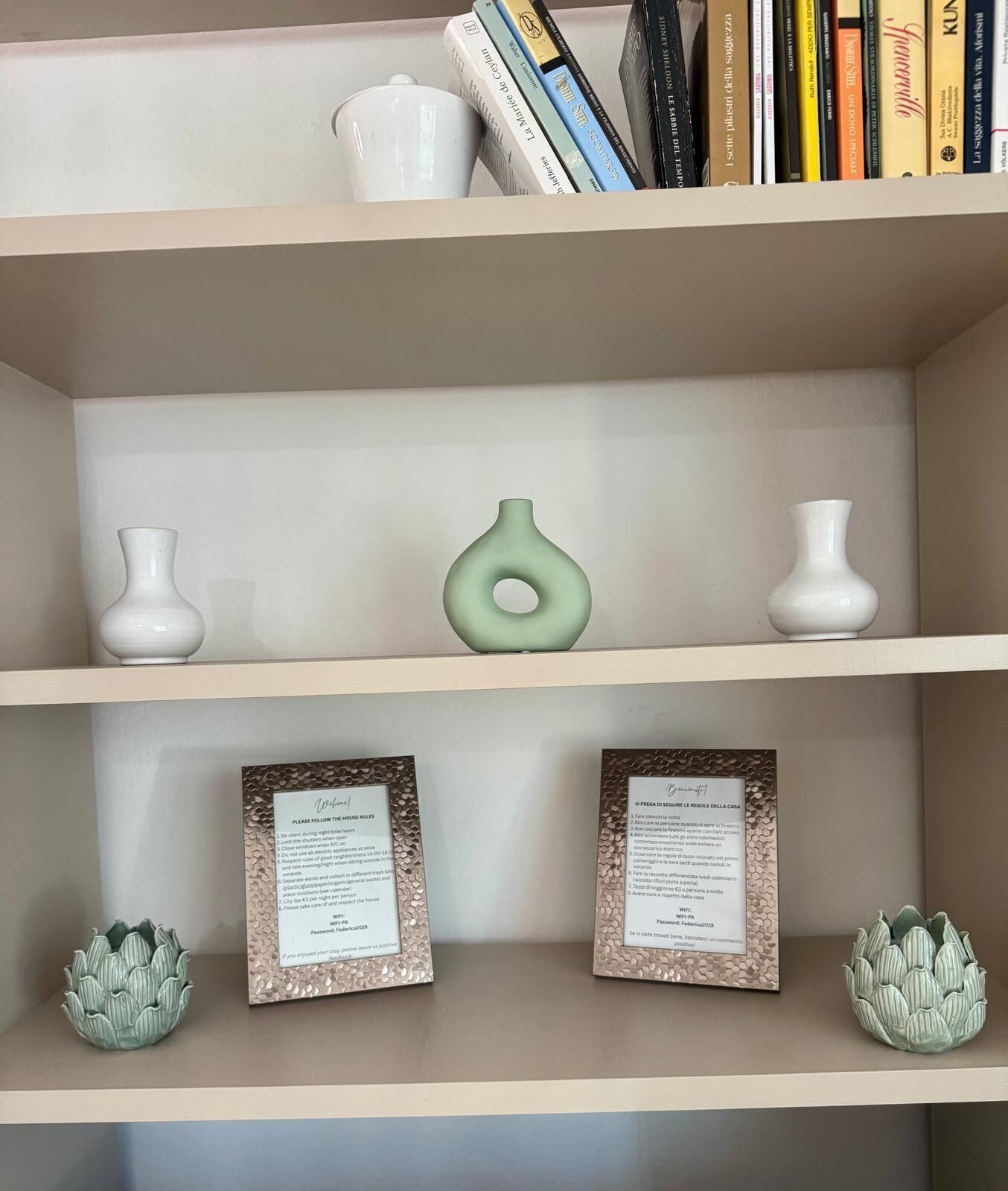 Uma estante com vasos decorativos, livros e placas com regras da casa emolduradas.