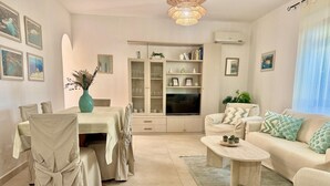 A living room with a sofa, coffee table, dining table with chairs, a TV, and a cabinet.