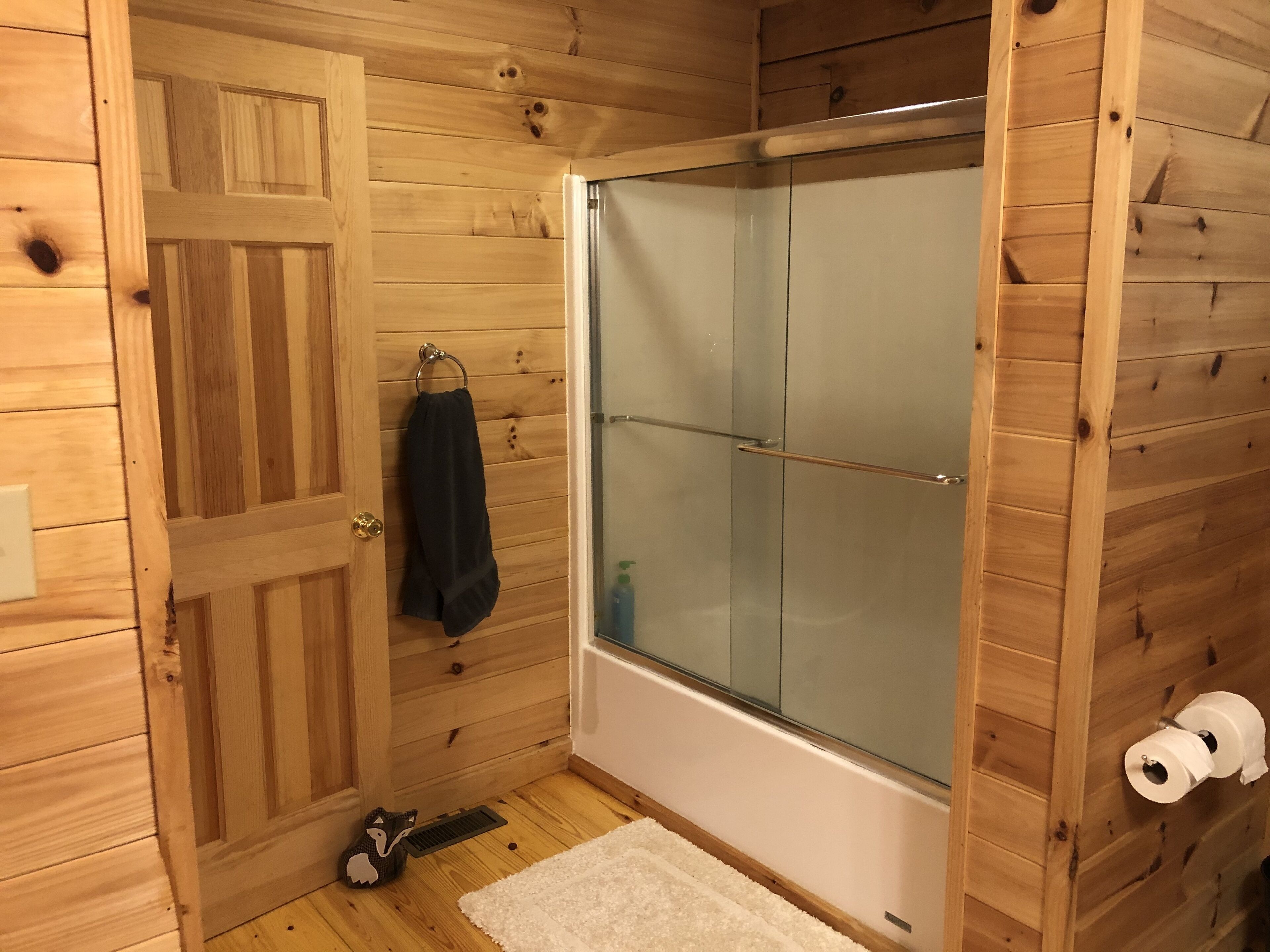 A wooden cabin bathroom with a glass shower enclosure, a towel rack, and a toilet paper holder.