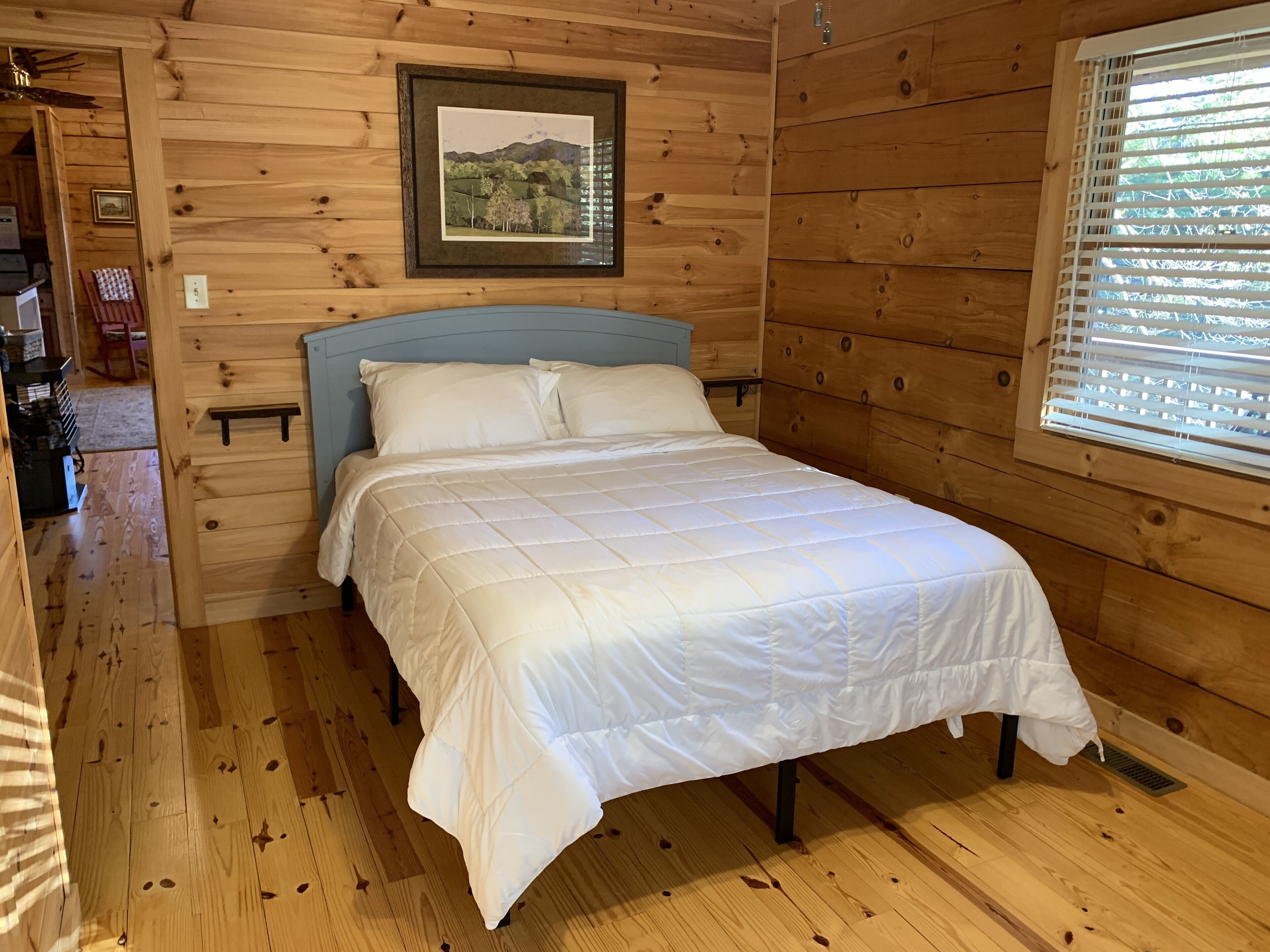 Een houten kamer met een bed, een lijst met een foto aan de muur en een raam met jaloezieën.