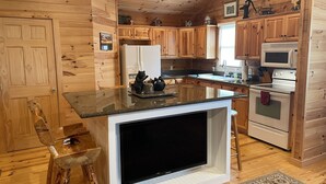 A kitchen with wooden cabinets, a granite countertop, a built-in TV, a refrigerator, a stove, and a microwave. - SUMMER SPECIAL — Book 5 nights 6+7th FREE — LOG CABIN with Privacy+ Firepit (West Jefferson)