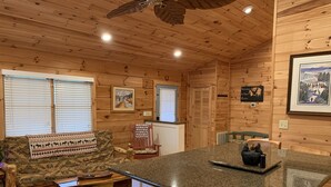 A cabin interior with a wooden ceiling, a kitchen island, a sofa with patterned cushions, and a rug. - SUMMER SPECIAL — Book 5 nights 6+7th FREE — LOG CABIN with Privacy+ Firepit (West Jefferson)