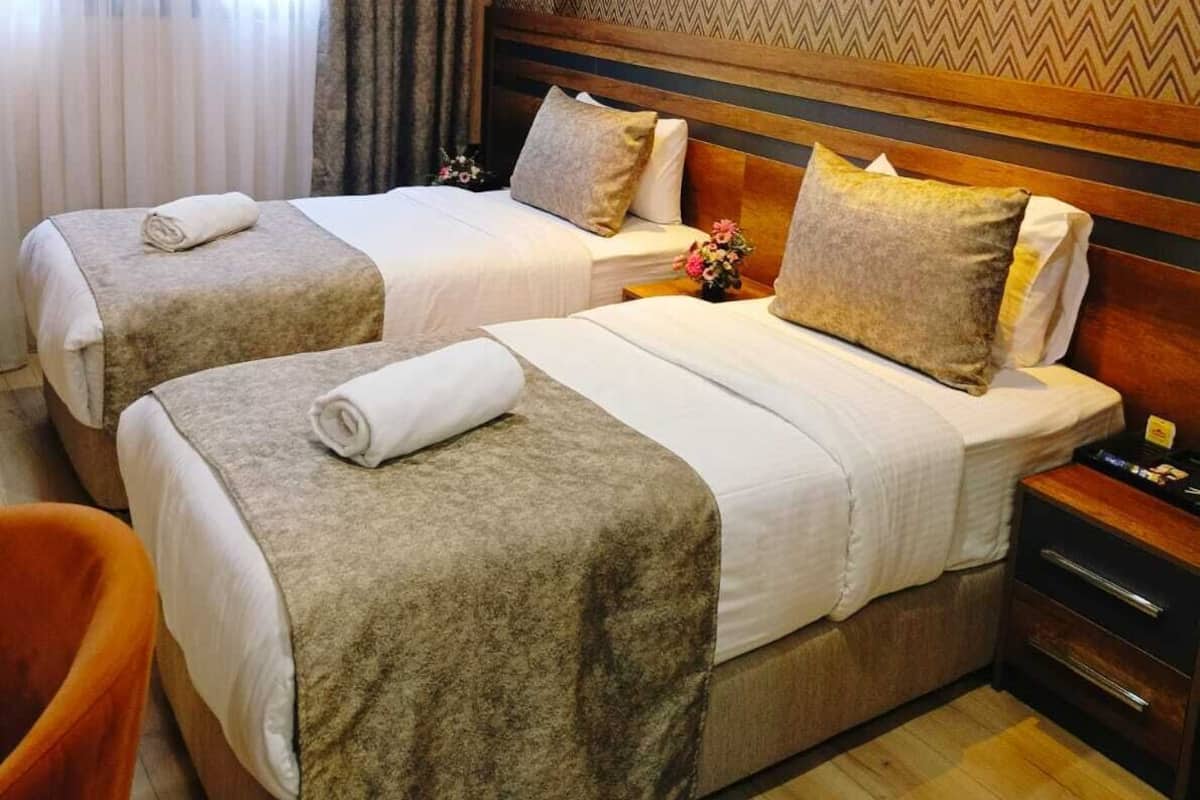 Ein Hotelzimmer mit zwei Betten, einem Holzkopfstück, einer Wand mit Muster und einem Fenster mit Vorhängen.