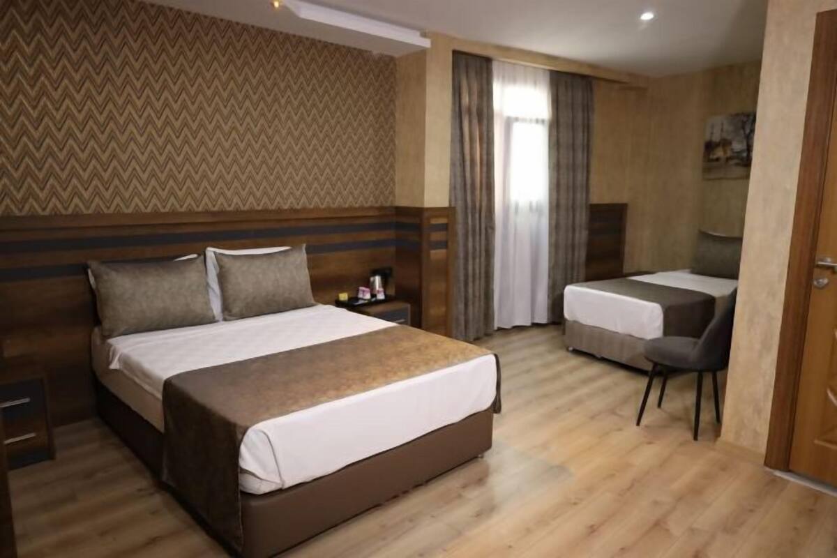 Ein Hotelzimmer mit einem großen Bett, einem kleineren Bett, einem Schreibtisch und einem Stuhl.