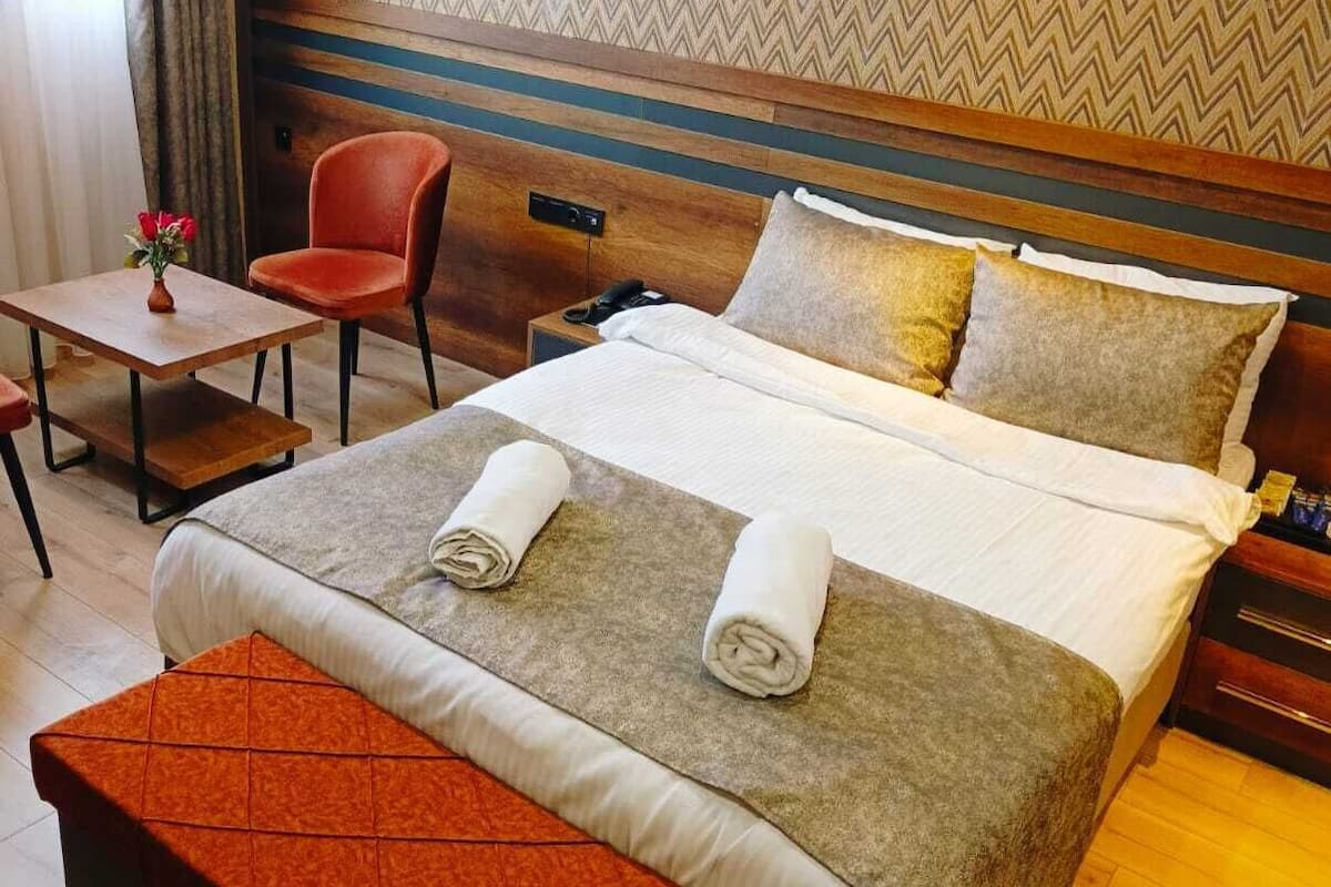 Ein Hotelzimmer mit einem großen Bett, einem Holzkopfstück, einem kleinen Tisch mit einem Stuhl und einer Bank.