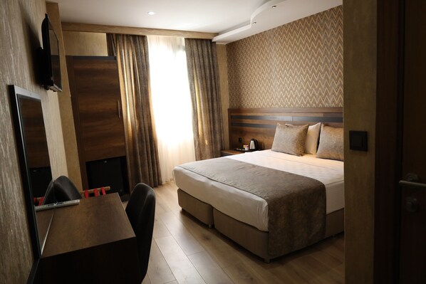 Una habitación de hotel con una cama grande, un escritorio con silla, un televisor montado en la pared y una ventana con cortinas.