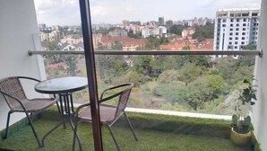 A balcony with a table and chairs, a small garden area, and a view of a cityscape. - Astoria Apartments (Nairobi)