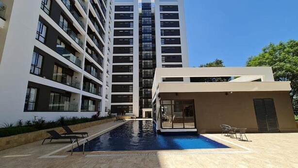 A modern building with a swimming pool, multiple balconies, and a covered area with chairs. - Astoria Apartments (Nairobi)