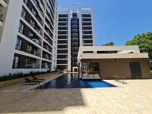 Un bâtiment moderne doté d’une piscine, de nombreux balcons et d’un espace couvert avec des chaises.