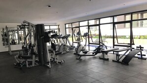 A gym with various exercise equipment, large windows, and a tiled floor. - Astoria Apartments (Nairobi)