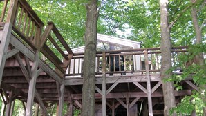 A wooden deck structure with railings, surrounded by trees.