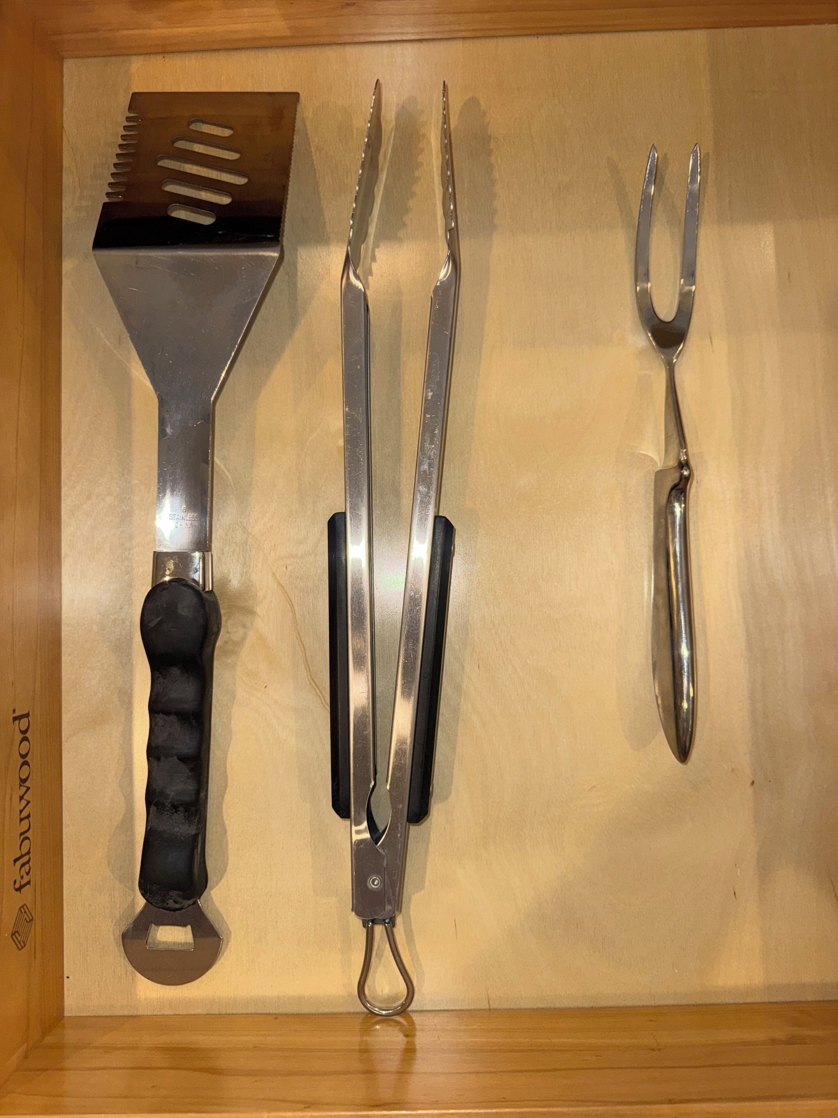 Ein Holzschrank mit drei Küchenutensilien: einem Pfannenwender, Küchenzangen und einer Schere.