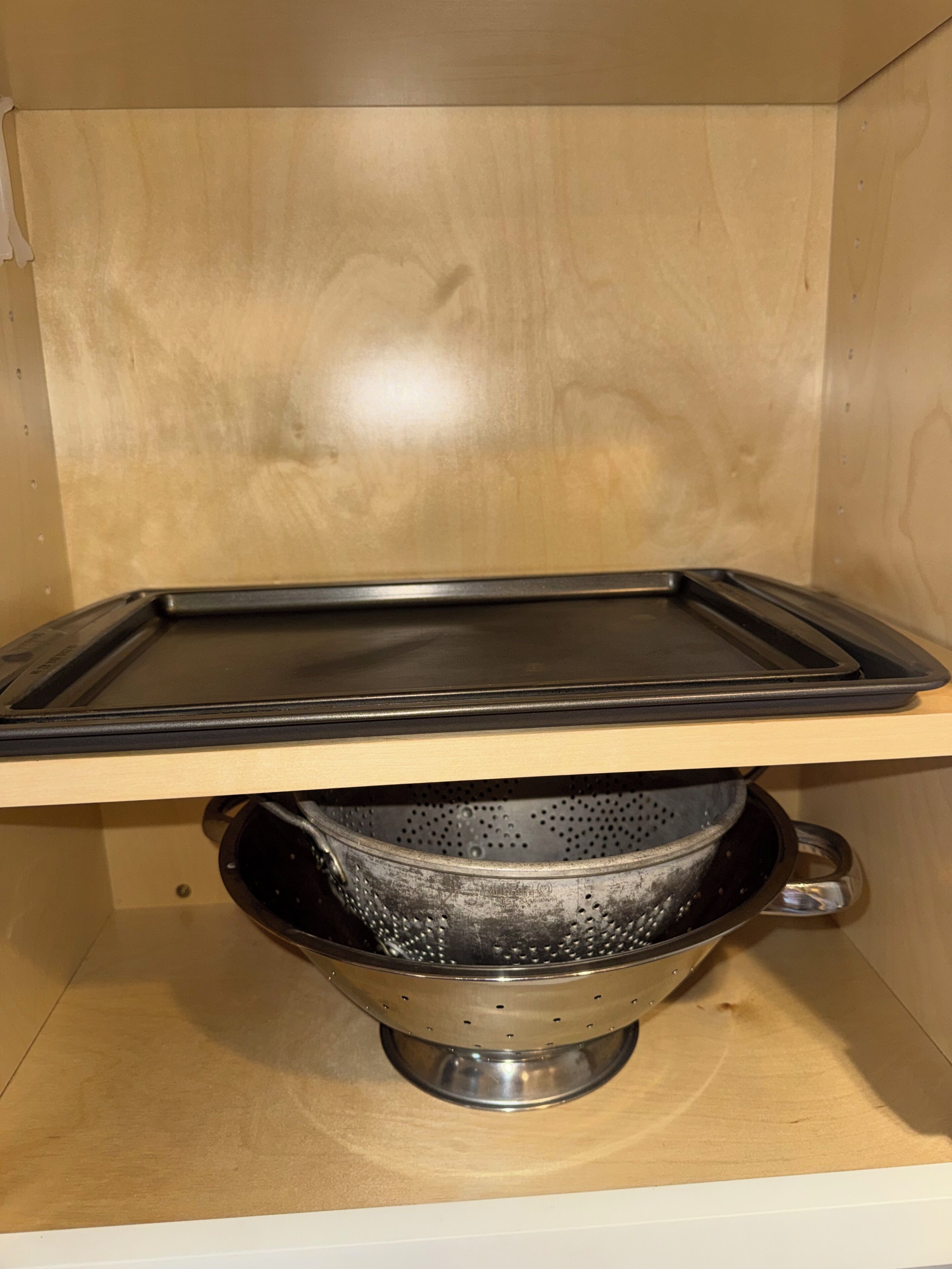 Una cocina con una bandeja negra sobre una encimera de madera, un colador de acero inoxidable y un armario de madera.