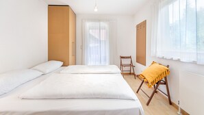Een kamer met twee bedden, een stoel, een radiator en een raam met gordijnen.