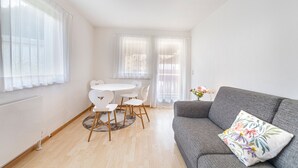 Een moderne woonkamer met een grijze bank, een ronde eettafel met witte stoelen en een radiator aan de muur.