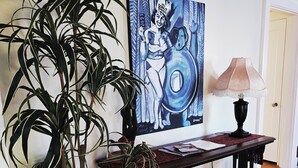 Ein Zimmer mit Holzboden, einer Topfpflanze, einem Tisch mit Lampe und einem Bild an der Wand.