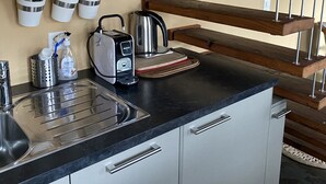 A kitchen with a black countertop, stainless steel sink, and wooden beams above. There are three white containers with utensils hanging on the wall.
