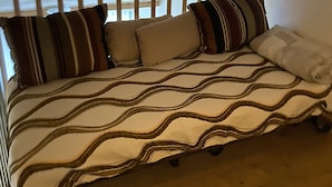 A bed with a patterned blanket and striped pillows in a room with wooden beams and a sloped ceiling.