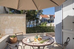 A round table with chairs, a potted plant, a glass of drink, and a plate with food. - Beach Residences Caroline (Hvar)