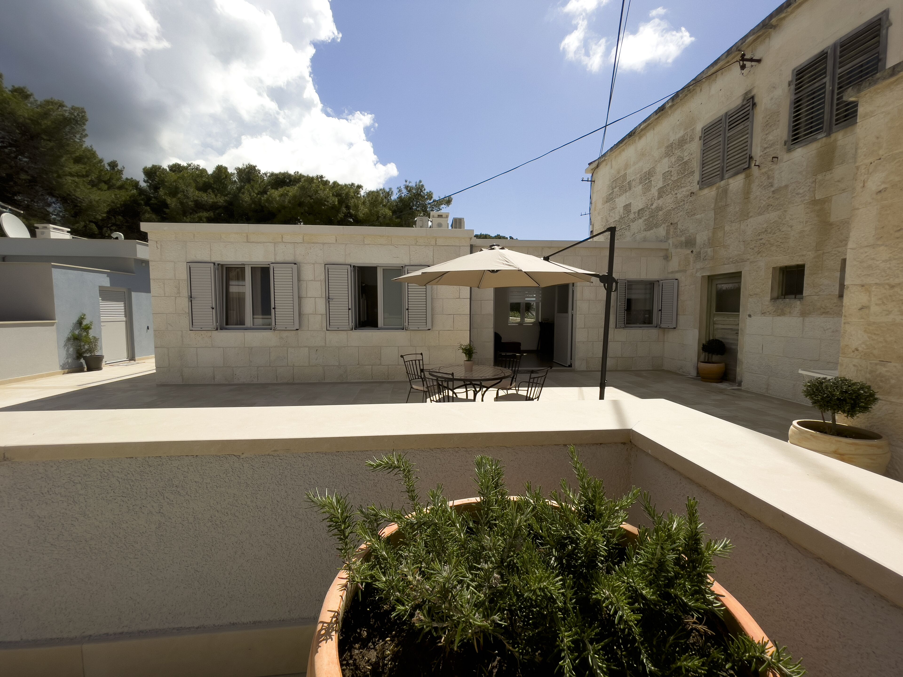 Un cortile con zona pranzo, una pianta in vaso e un edificio con pareti in pietra e persiane.