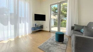 Una sala de estar moderna con un televisor de pantalla plana, un sofá gris y un reposapiés azul.