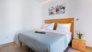 Una cama bien hecha con cabecera de madera, una mesita de noche con una planta y un cuadro en la pared.